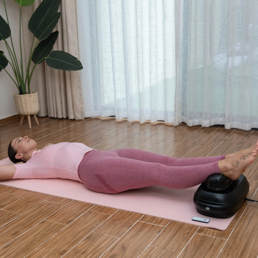 Femme allongée sur le dos, détendue, les chevilles posées sur la machine chi FlowMotion, dans un salon lumineux
