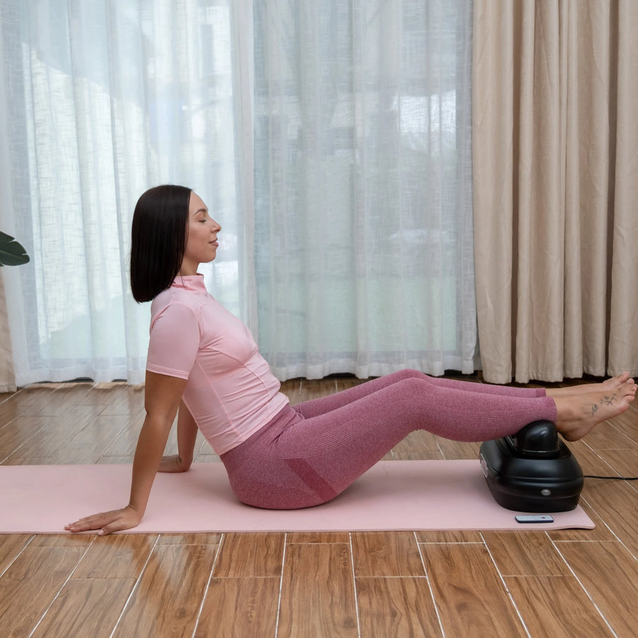 Femme assise, détendue, sur un tapis de yoga, les jambes posées sur la machine chi FlowMotion
